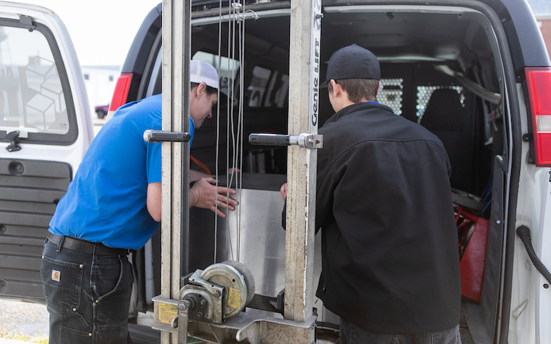 Two company technicians loading a heavy ice machine into the back of a company van to be delivered